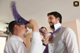 At the groom's parents' home near Toulouse in Haute-Garonne, one of the groomsmen diligently assists with the final preparations by adjusting the groom's tie knot before the wedding ceremony.